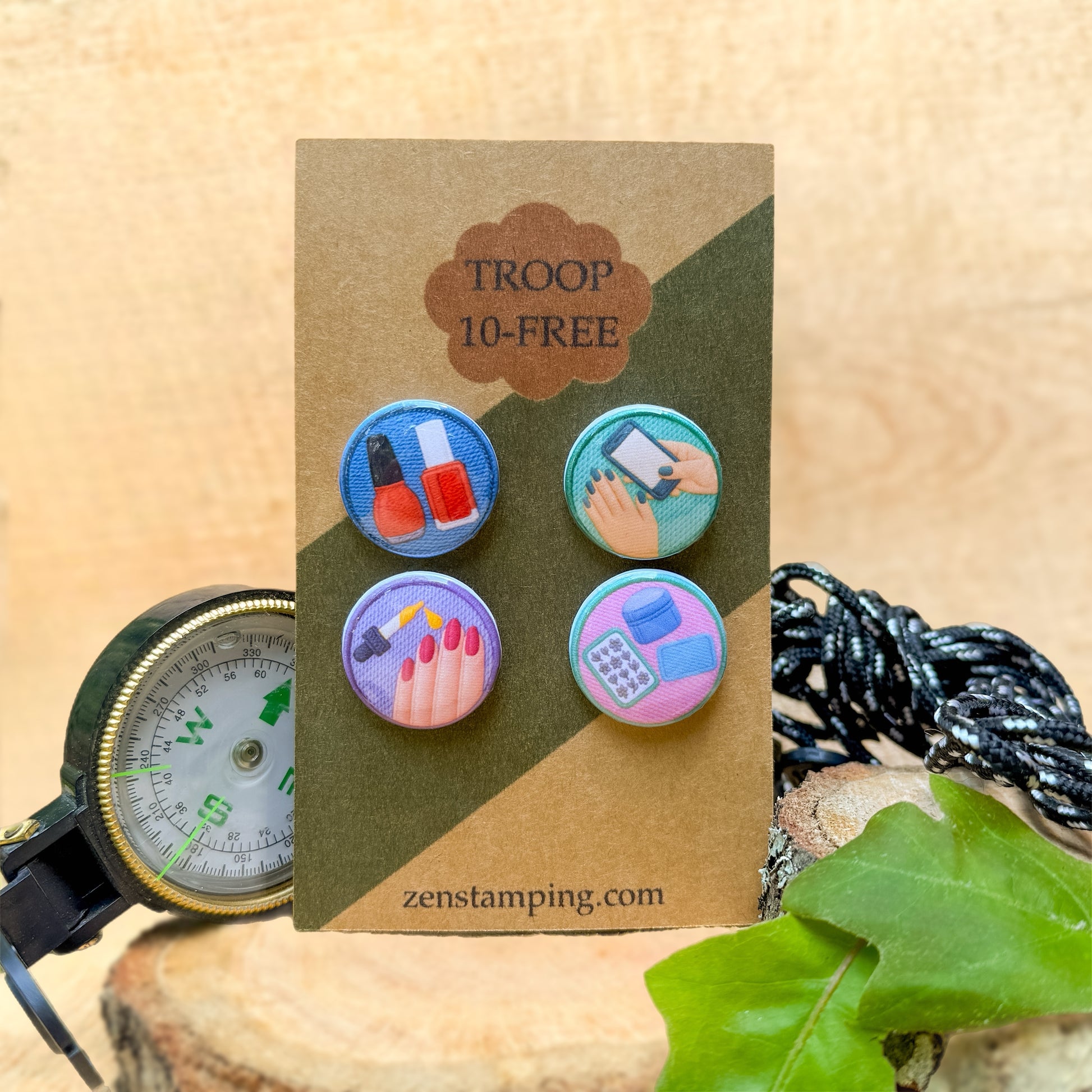 Set of colorful buttons on a Troop 10-Free card with a compass and leaf in the background