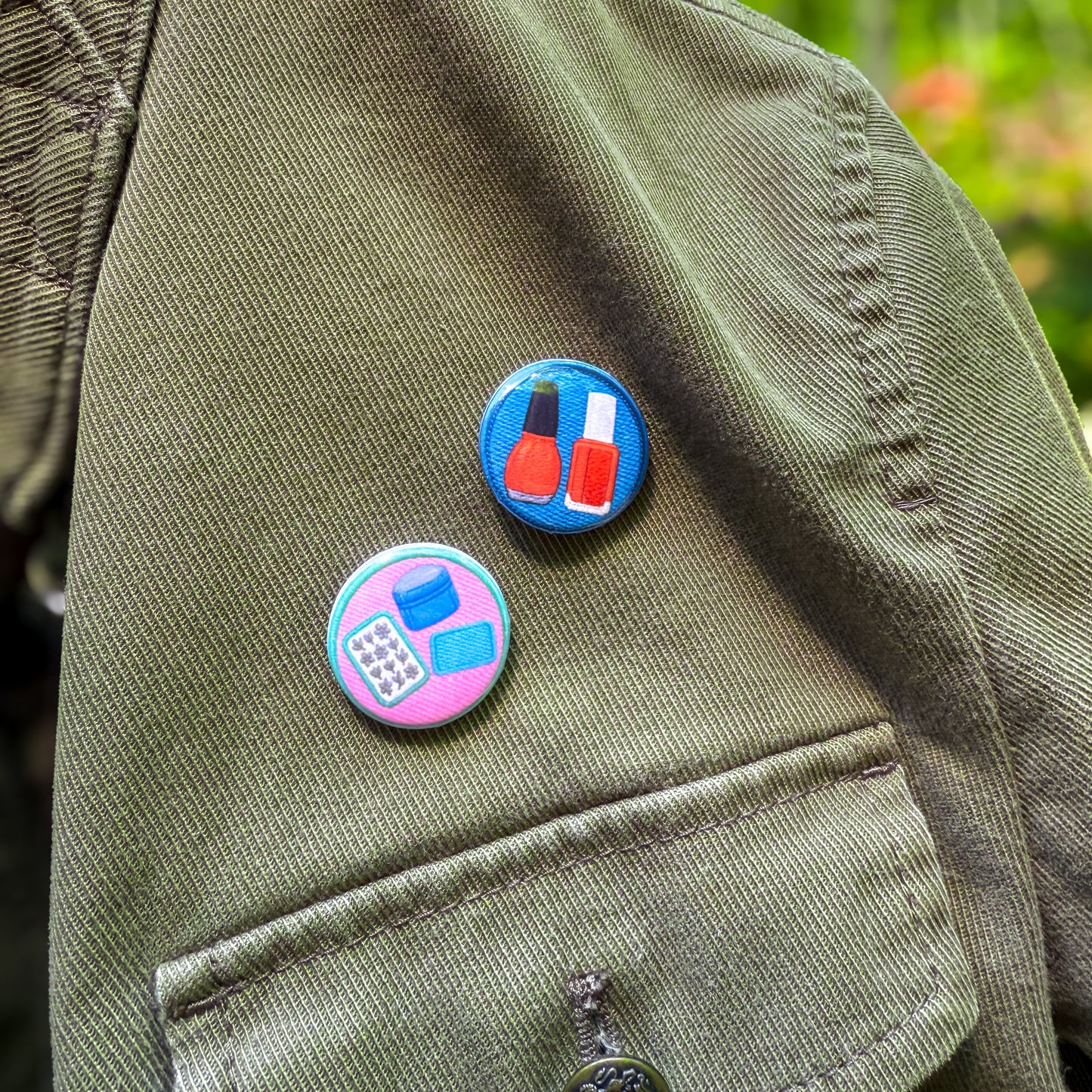 Two colorful pins on a green jacket with a blurred natural background