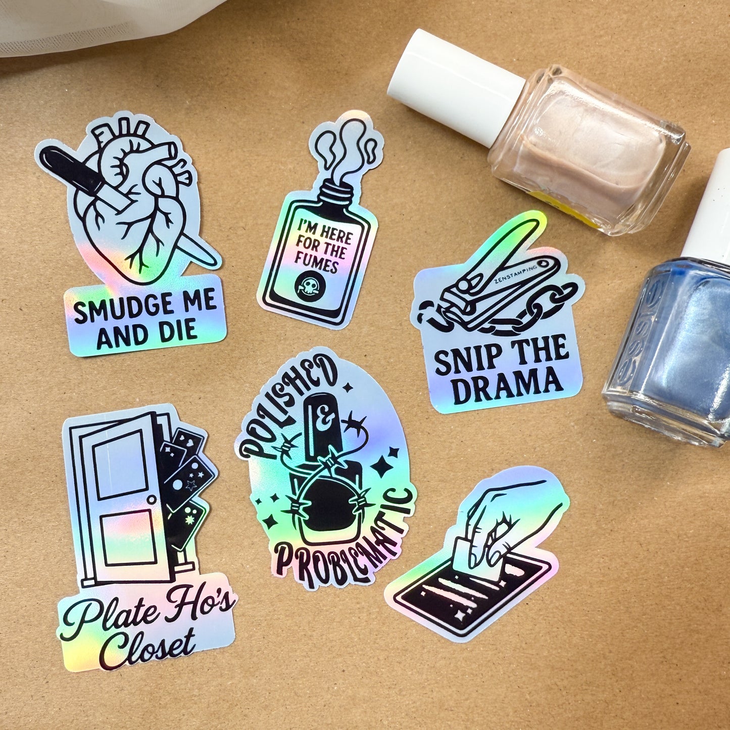 Holographic stickers with various designs and text on a brown surface with nail polish bottles.