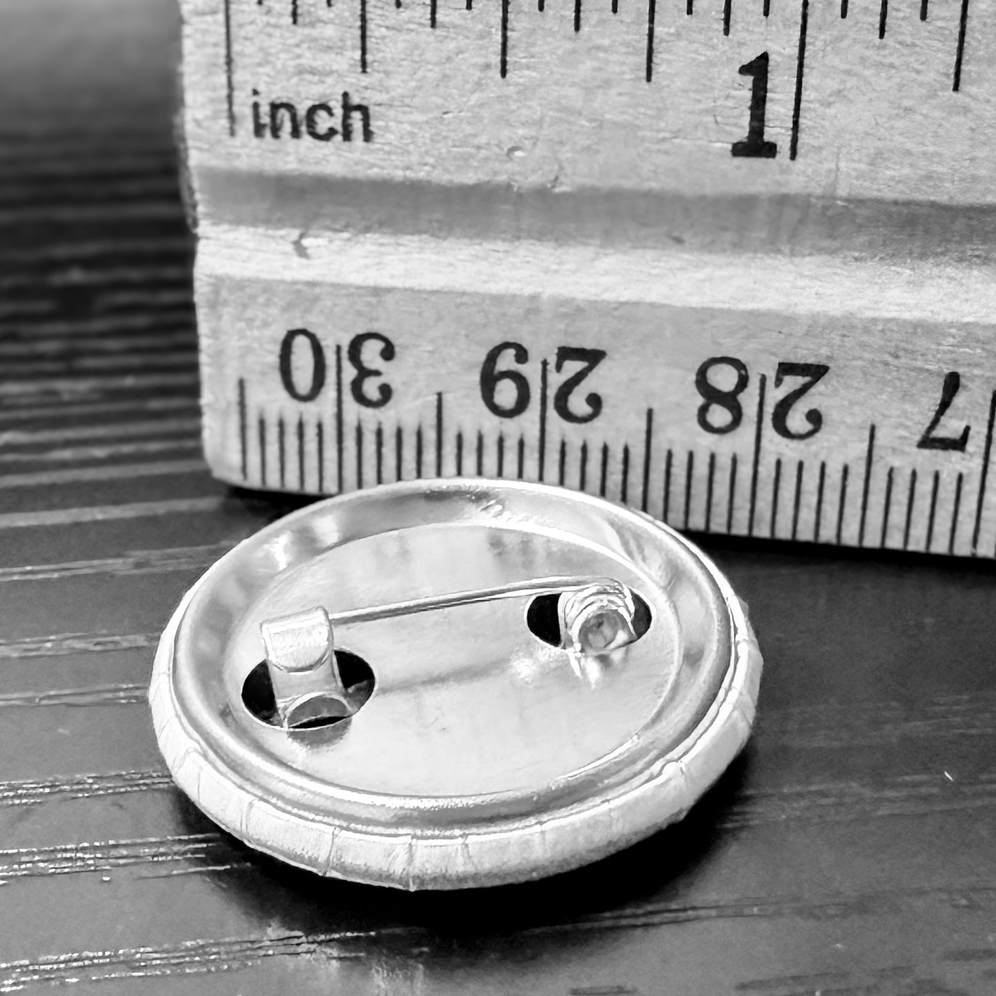 Metallic brooch on a wooden surface with a ruler for scale.