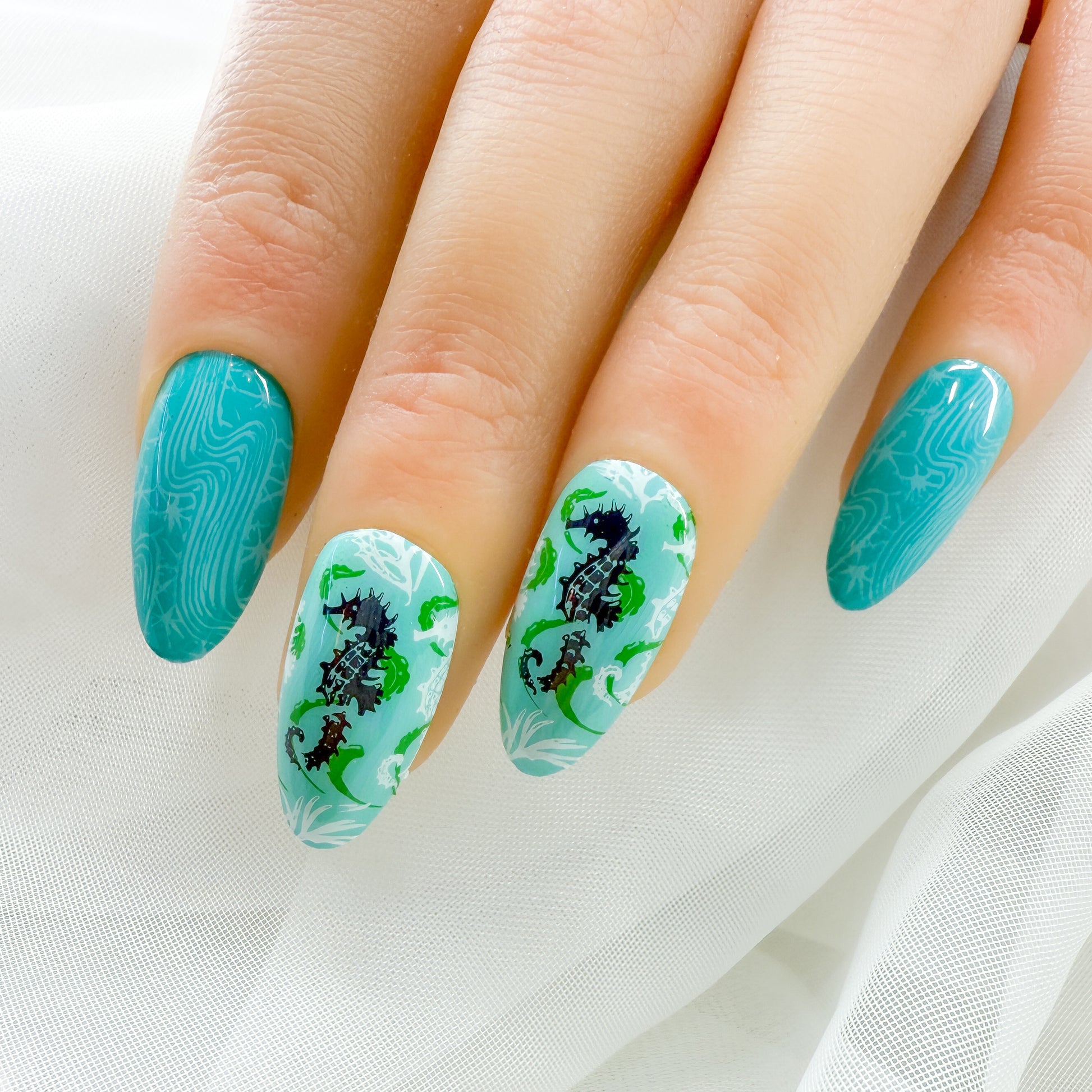 Nails with teal and white marbled design featuring seahorses on a white background