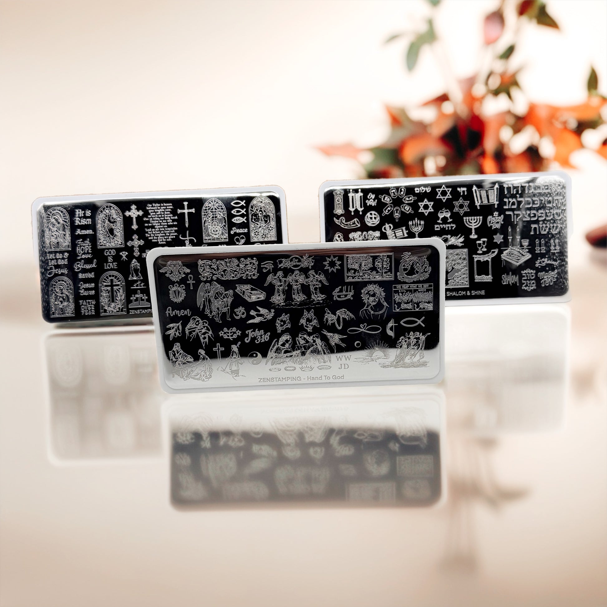 Three stainless steel stamping plates with white designs on a reflective surface.